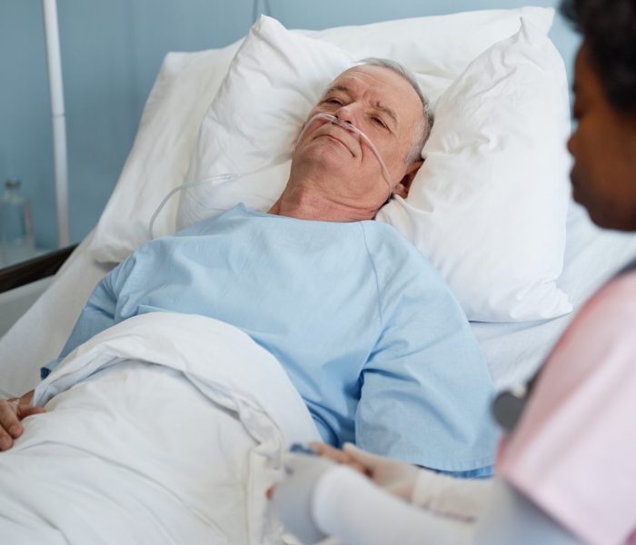Elderly man lying in hospital bed with attendant nearby discussing medical details, sharing empathy and care for patients well-being, and critical health recovery